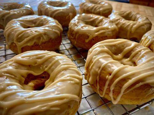 A close-up of freshly glazed donuts on a cooling rack, showcasing a creamy icing drizzled on top.