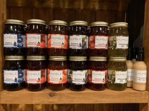 A wooden shelf displaying jars of various jams and sauces, labeled "HUMBLE," in different flavors.