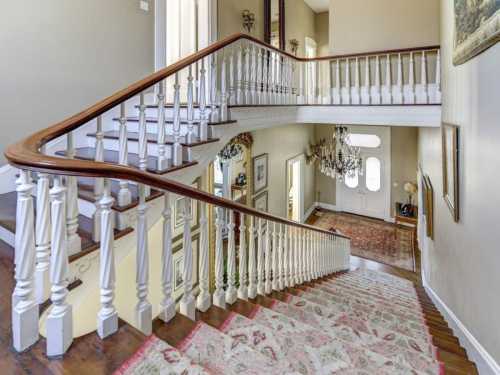 A spacious staircase with a wooden railing, leading down to a well-lit foyer adorned with rugs and artwork.