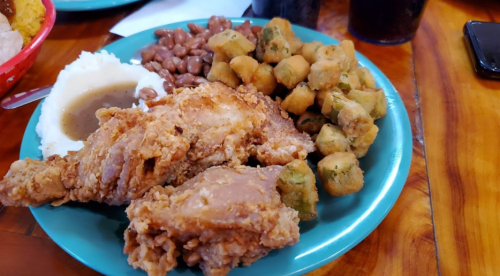 A plate of fried chicken, mashed potatoes with gravy, pinto beans, and fried okra on a wooden table.