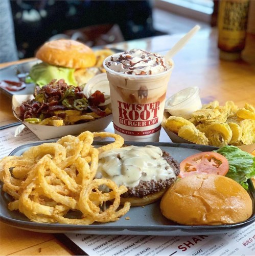 A plate of onion rings, a cheeseburger with toppings, a side of pickles, and a milkshake on a table.