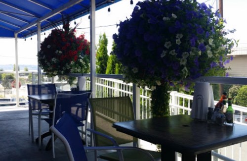 Outdoor dining area with tables and colorful hanging flower baskets under a blue awning.
