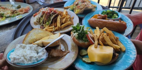 A variety of dishes on plates, including burgers, hot dogs, fries, and a salad, served on a large tray.