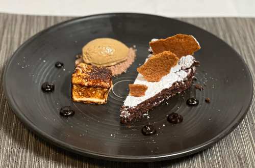A black plate featuring a slice of chocolate cake, a scoop of coffee ice cream, and a small dessert with caramel.