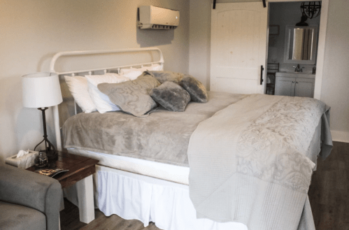 Cozy bedroom featuring a large bed with gray bedding, decorative pillows, and a small side table.