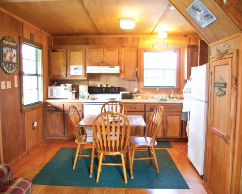 Cozy wooden kitchen with a dining table, chairs, and appliances, featuring warm lighting and rustic decor.