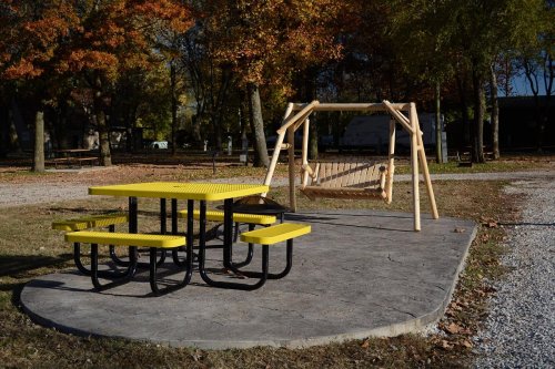 A yellow picnic table and a wooden swing set in a park with autumn trees in the background.