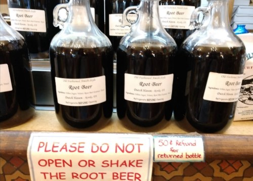 Several glass jugs of root beer on display, with a sign warning not to open or shake them and offering a bottle refund.