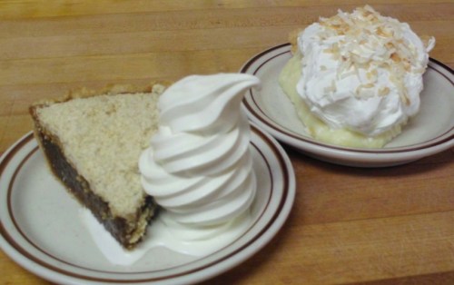 A slice of pie with a swirl of soft serve ice cream and a bowl of whipped cream topped with toasted coconut.