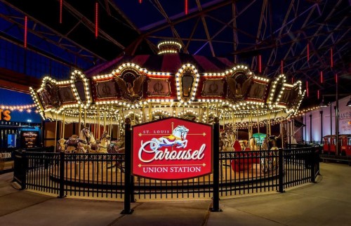 A brightly lit carousel at Union Station in St. Louis, featuring ornate horses and a welcoming sign.