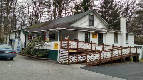 A small, two-story building with a wooden ramp, surrounded by trees and a parking area.