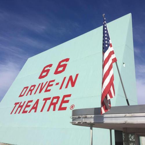 A turquoise building with "66 Drive-In Theatre" in bold red letters and an American flag on a pole.