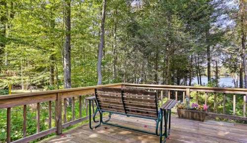 A wooden deck with a bench overlooks a lush green forest and a serene body of water in the background.