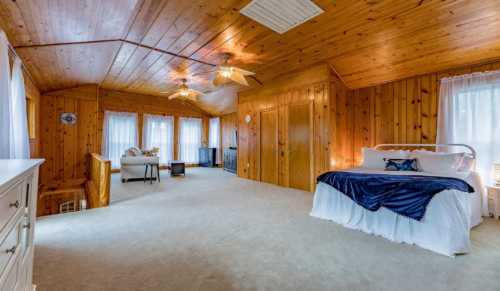 Spacious room with wooden walls, a large bed, and seating area, featuring natural light from multiple windows.