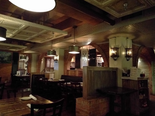 Cozy restaurant interior with wooden tables, brick walls, and warm lighting from hanging lamps and wall sconces.