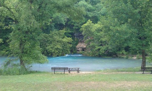 A serene river scene surrounded by lush greenery, with benches overlooking the water.