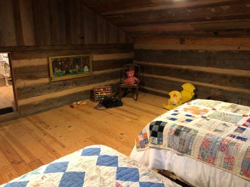 Cozy attic bedroom with two quilted beds, wooden walls, and a rocking chair, featuring a playful decor.
