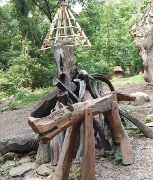 Wooden sculptures of animals surrounded by trees in a natural setting, with a unique structure overhead.