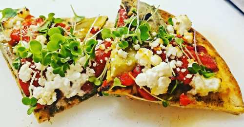 Two slices of pizza topped with tomatoes, green peppers, feta cheese, and microgreens on a white plate.