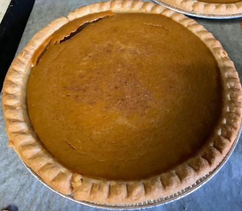A freshly baked pumpkin pie with a golden-brown crust, resting on a baking sheet.
