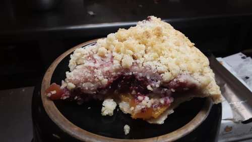 A slice of pie with a crumbly topping, revealing a colorful fruit filling, served on a black plate.