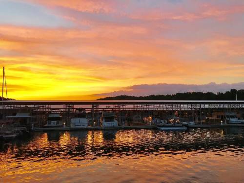A vibrant sunset over a marina, with boats docked and colorful reflections on the water.