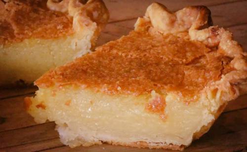 A slice of golden, flaky pie with a creamy filling, resting on a wooden surface.