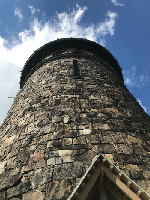 A tall stone tower viewed from below, with a blue sky and clouds in the background.