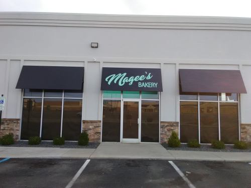 Exterior of Magee's Bakery, featuring a sign and large windows, with a landscaped entrance and awnings.