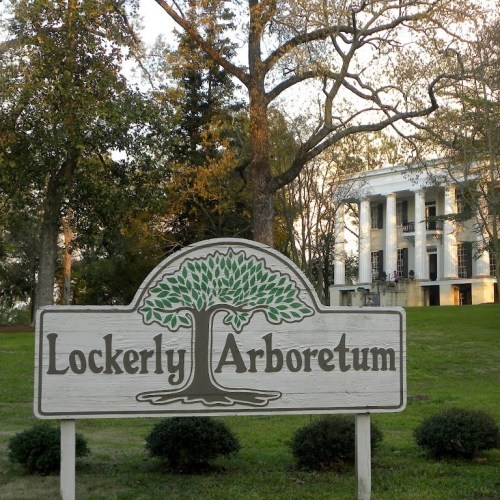 Sign for Lockerly Arboretum in front of a historic building surrounded by trees and greenery.