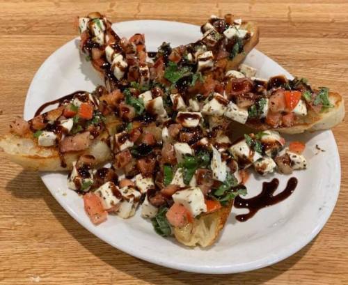 A plate of bruschetta topped with diced tomatoes, mozzarella, basil, and balsamic drizzle on toasted bread.