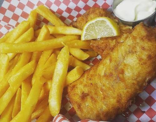 A plate of golden fried fish with a lemon wedge, served alongside crispy French fries and a small cup of tartar sauce.