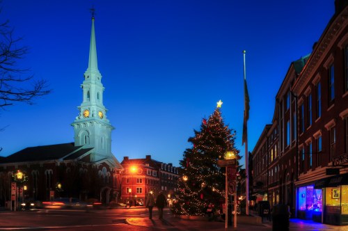 A festive scene featuring a lit Christmas tree and a church steeple against a twilight sky.