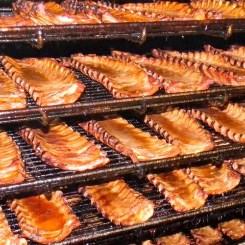 Smoked ribs arranged on multiple racks in a smoker, showcasing a rich, caramelized glaze.