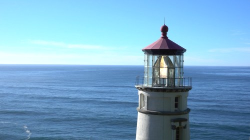A lighthouse with a red roof stands tall against a clear blue sky and calm ocean waters.