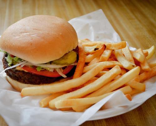 A hamburger with lettuce, tomato, and pickles, served with a side of golden French fries on a paper plate.