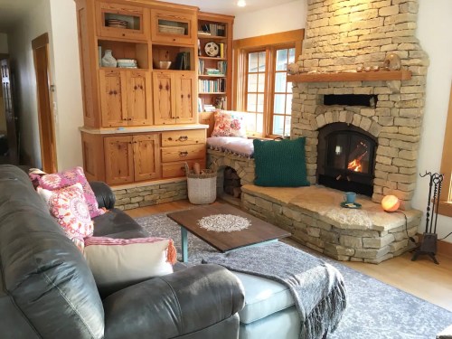 Cozy living room with a stone fireplace, wooden furniture, and a comfortable sofa adorned with colorful pillows.