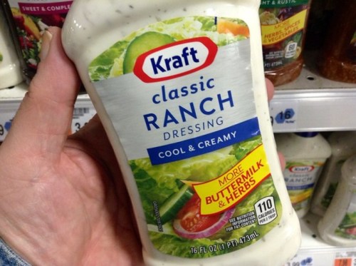 A person holding a bottle of Kraft Classic Ranch Dressing in a grocery store aisle.