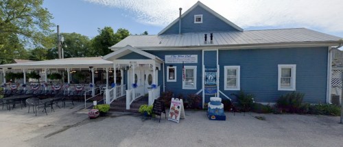 A blue building with a porch, outdoor seating, and patriotic decorations, labeled "The Blue Owl."