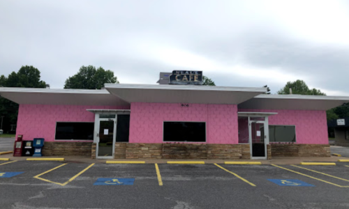 A pink cafe building with a sign reading "Neal's Cafe," featuring large windows and a parking lot in front.