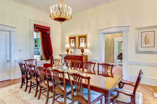 Elegant dining room featuring a long wooden table, chandelier, and classic decor with red curtains and framed art.