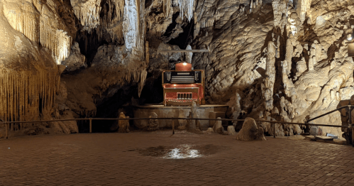 A cavernous space with stalactites and stalagmites, featuring a red organ at the center and soft lighting.