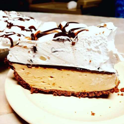 A slice of creamy pie with a graham cracker crust, topped with whipped cream and chocolate drizzle.