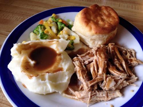 A plate of food featuring pulled pork, mashed potatoes with gravy, mixed vegetables, and a biscuit.
