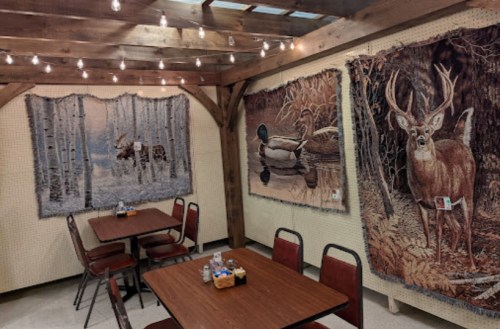 Cozy dining area with wooden beams, string lights, and nature-themed tapestries featuring deer, ducks, and a moose.