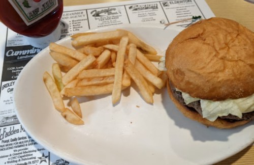 A plate with a sandwich and fries, accompanied by a bottle of ketchup on a table with a menu underneath.