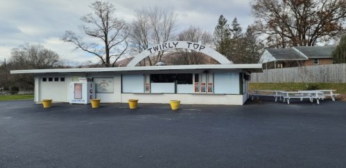 A retro ice cream stand named "Twirly Top" with a white exterior and picnic tables outside, set in a quiet area.