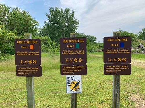 Three trail signs at a park, detailing Quartz Lake, Sand Prairie, and Agate Lake trails with length and difficulty information.