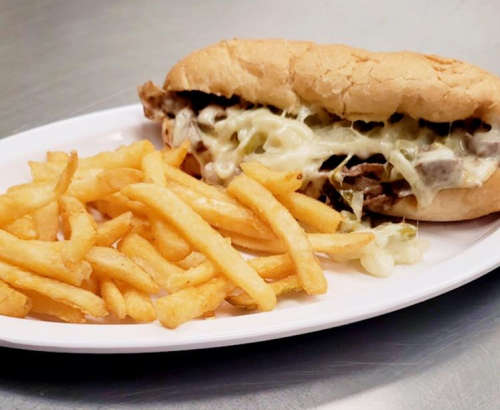 A plate with a cheesy steak sandwich and a side of golden French fries.