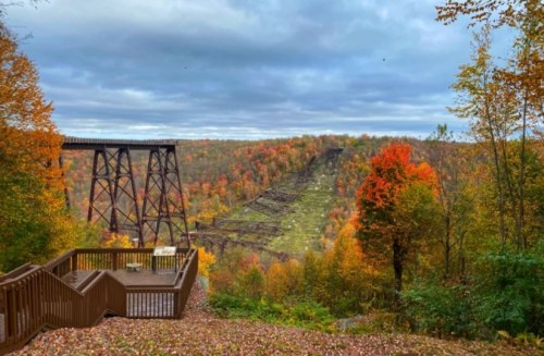 A scenic view of a colorful autumn landscape with a bridge and a hillside covered in vibrant fall foliage.
